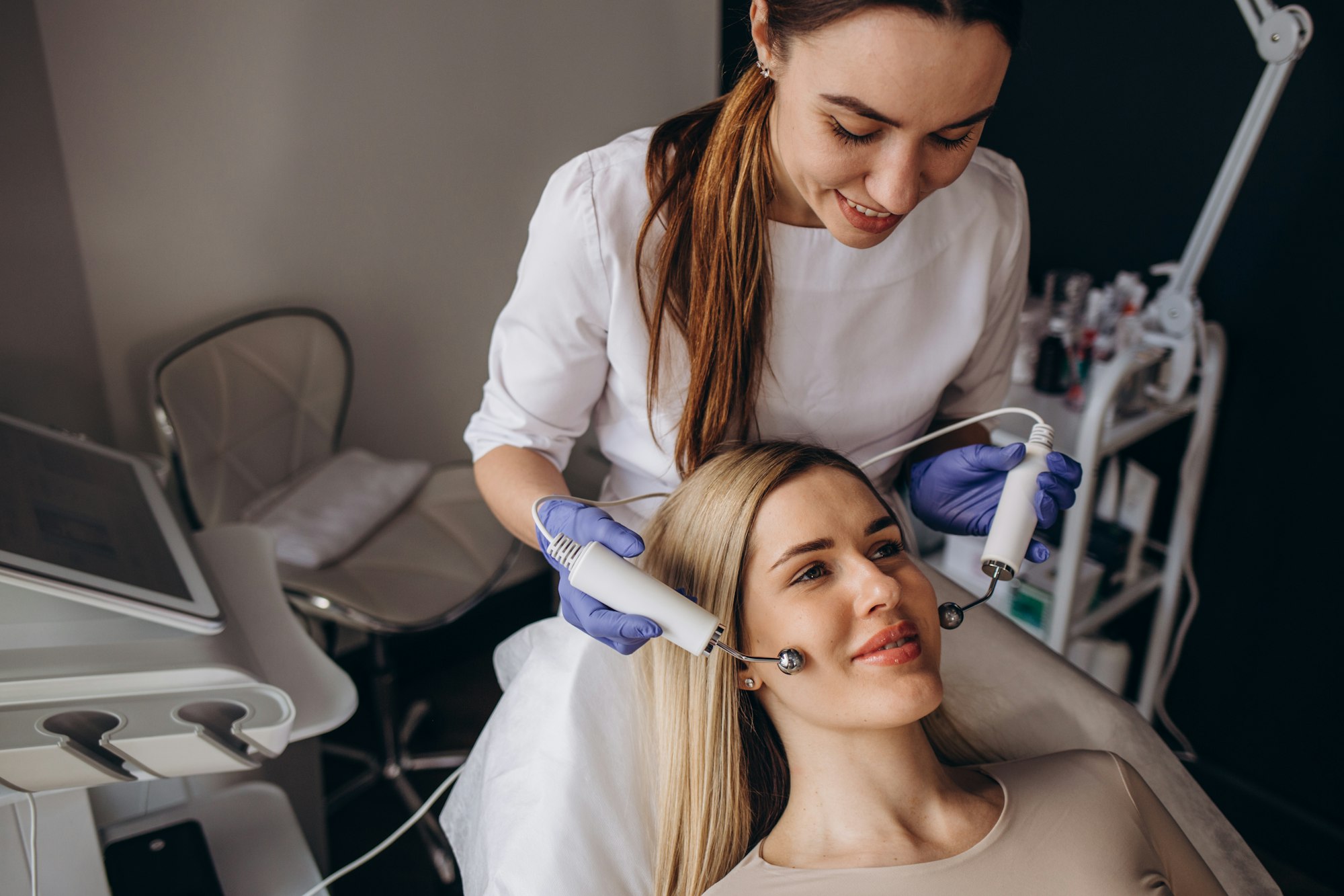 A doctor cosmetologist makes a microcurrent facial therapy to a young woman with a device