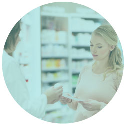 woman in a pharmacy reviewing a prescription with the pharmacist with shelves of medication in the background